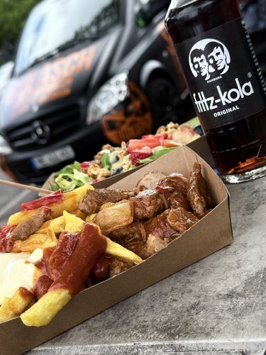 Currywurst-Pommes-Teller und bunter Fruchtsalat vor dem Foodtruck